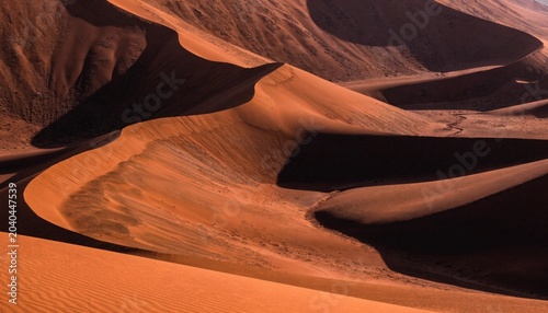 Fotografie Dramatic, towering dunes of deep orange and red, with shadows creating dynamic patterns