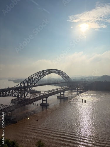 Majestic steel arch bridge crossing a wide river under bright midday sun and blue sky