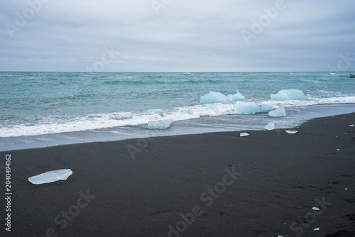 Canvas Print Black sand beach with scattered icebergs and waves under an overcast sky,Jokulsa