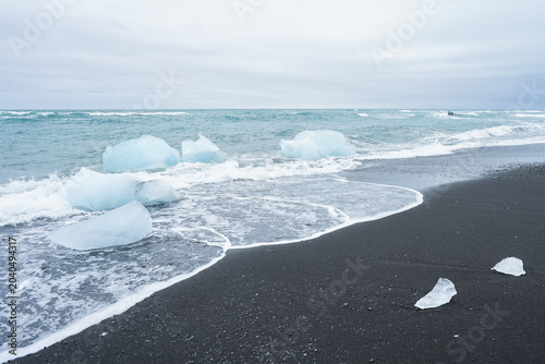 Foto Icebergs washing ashore on a black sand beach with waves and ocean in the backgr