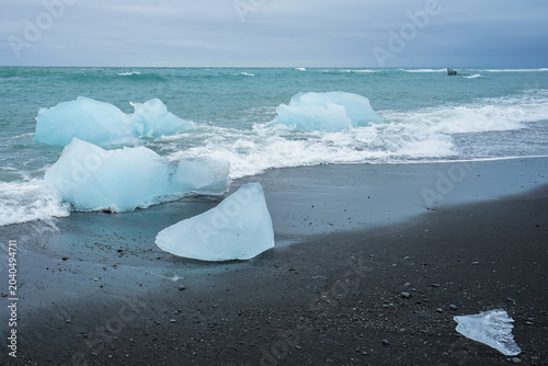 Obraz na płótnie Icebergs washed ashore on a black sand beach with ocean waves in the background,
