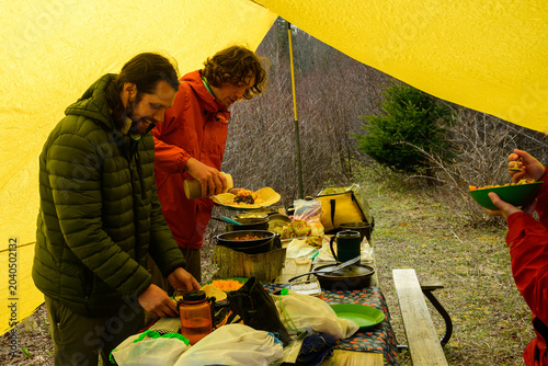 Bild auf Leinwand Two wilderness guides preparing burrito dinner under a yellow tarp shelter at a