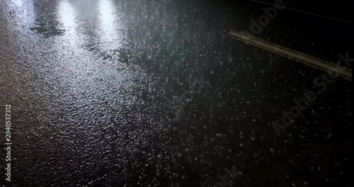 Close up of cars, tuk-tuks, and other vehicles speeding through heavy rain at night across wet, reflective asphalt.