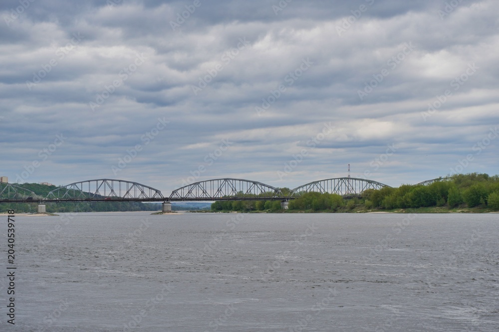 Fototapeta premium Steel arched bridge over a wide river under cloudy dramatic sky