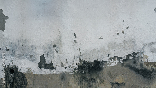 Abstract textured background of a weathered white wall with severe peeling paint and dark moisture stains