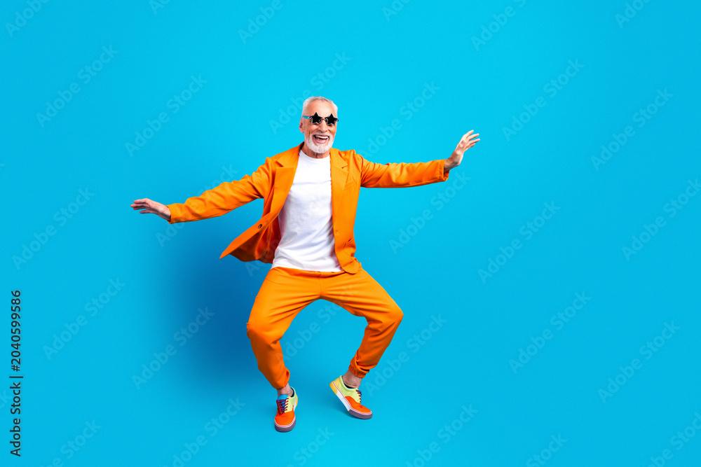 Fototapeta premium Senior man in bright orange suit dancing and smiling on blue background, joyful active lifestyle and colorful fashion portrait