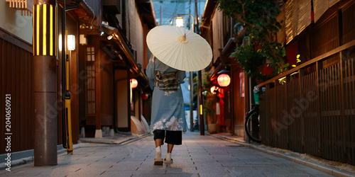Woman in blue kimono with wagasa umbrella walking in traditional Gion alley at dusk, Kyoto, Japan