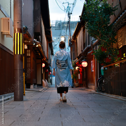 Woman in blue kimono walking in traditional Gion alley at dusk with red lanterns, Kyoto, Japan