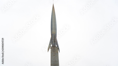 Canvas Print Metal rocket stands tall against stark white sky
