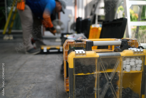 Φωτογραφία Yellow Plastic Tool Organizer Cases on Ground with Blurred Worker in Background