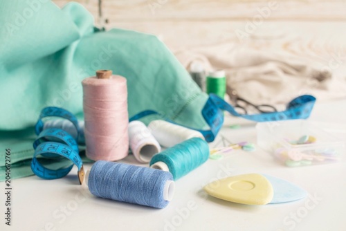 Sewing supplies on a white table with a sewing machine in the background. Sewing machine with fabric and sewing accessories on a white table.
