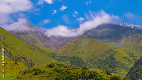 Time-lapse of white clouds flow on blue sky above green mountains in rural Kyrgyzstan at sunny summer day.