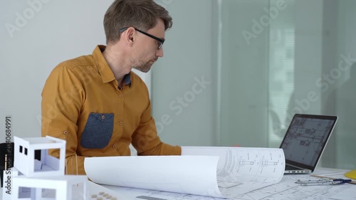 Architect carefully assembling a scaled architectural model, designing and planning a new building project on a desk with blueprints, engineering tools, and construction safety helmet