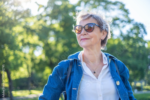 Elegant senior woman in sunglasses looking into distance on sunny day, active retirement travel and vitality lifestyle concept in spring and summer with copy space
