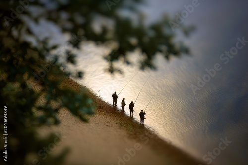 High angle view of four people fishing on a sandy shore. Silhouettes of anglers with a creative tilt-shift miniature effect. Group hobby and outdoor recreation concept