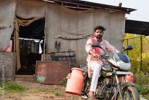 Tableau sur toile Young rural man riding a motorcycle with a milk container in a village setting
