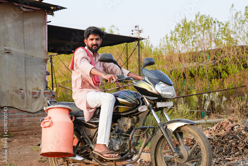 Tableau sur toile Young rural man riding a motorcycle with a milk container in a village setting