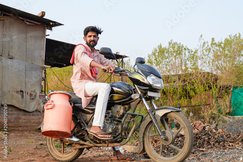 Fotografie Young rural man riding a motorcycle with a milk container in a village setting