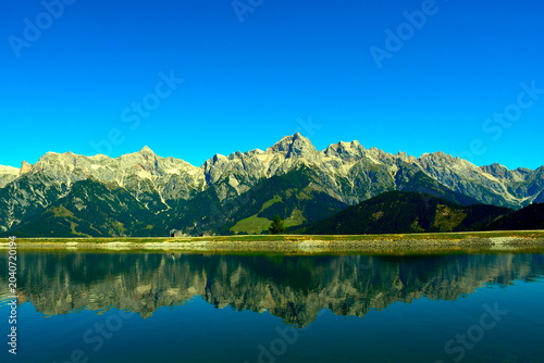 Canvas Print Ein gewaltiger Bergkamm in den Alpen spiegelt sich im ruhigen Wasser des vorgelagerten Bergsees