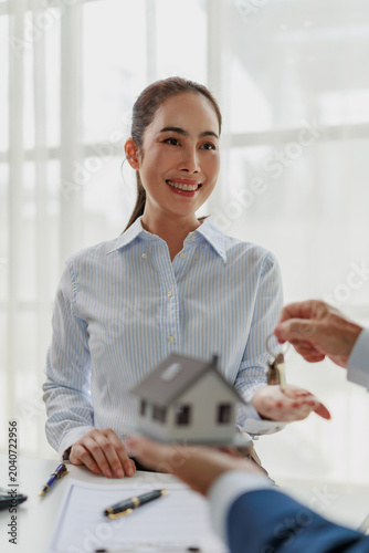 Schilderij op canvas Woman smiling while receiving keys and a house model from an agent, representing