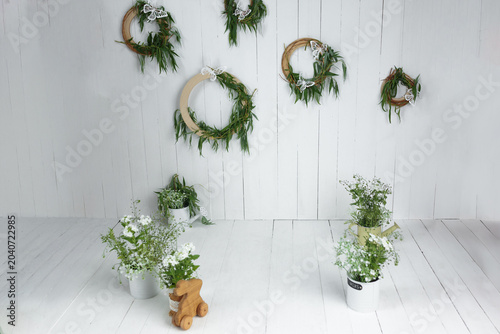 White wooden wall and floor with green wreaths and potted plants