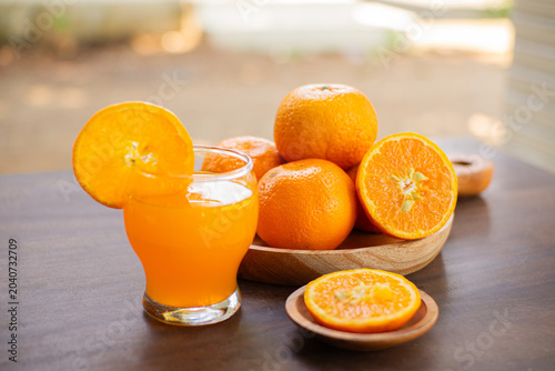 Fresh cut oranges on a wooden plate with a bottle and a glass of fresh orange juice on a outdoor table