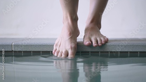 Bare feet of a person poised at the edge of a pool, gently touching the water surface, creating ripples as they prepare to step into the cool water