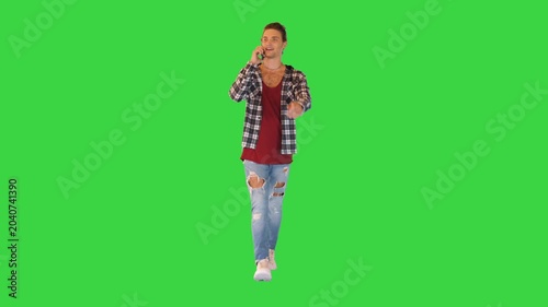 Attractive young man in contemporary outfit walks talking on the phone on a Green Screen, Chroma Key.