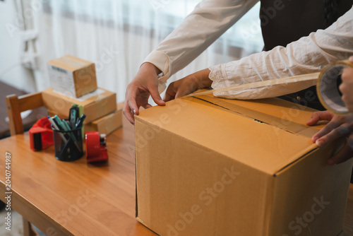 Teamwork sealing cardboard box with adhesive tape during package preparation shipping logistics workflow ecommerce business operations