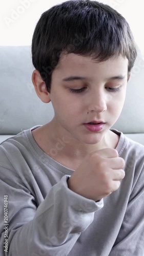 Child sitting on sofa at home and holding hand on chest. Male having asthma attack, difficulties with breathe, feeling severe pain or dyspnea