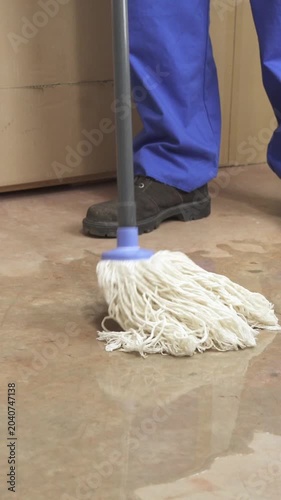 Male worker cleaning-up a slip hazard on the floor of an industrial plant with white mop.