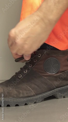 Close-up of a manufacturing worker's hands tying the laces on his work boots in a factory.