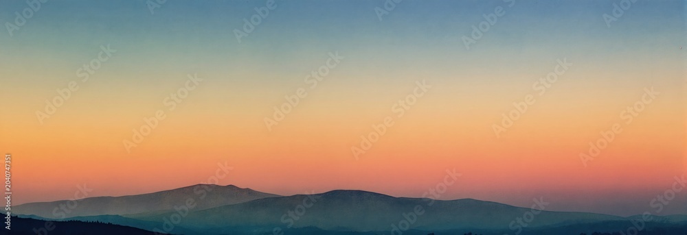 Obraz premium Soft gradient sky painted with warm sunrise colors over distant mountain ranges. Peaceful natural landscape in watercolor style. Calm atmosphere for relaxation and serenity.