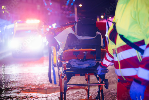 Fotografie Paramedic pulling stretcher with medical equipment from emergency ambulance on city street at night