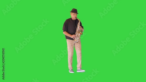 An elderly man walks in a funny manner playing the saxophone on a Green Screen, Chroma Key.