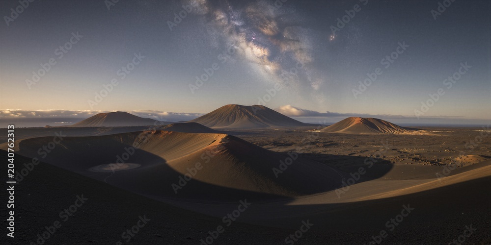 Fototapeta premium A panoramic view of volcanic cones under a starry sky at twilight in a barren desert environment captures the serene and majestic beauty of the Milky Way's galactic core.