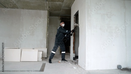 Photography Worker demolishing interior brick wall with sledgehammer at construction site