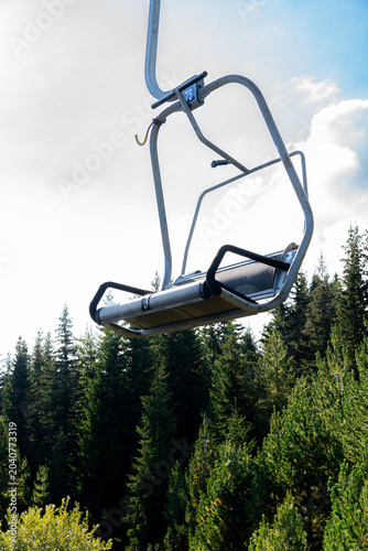 Canvas Print Empty chairlift cabin moving over green pine trees and mountain forest against a