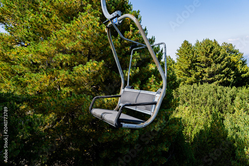 Schilderij op canvas Empty chairlift chair moving over pine trees and green forest in the mountains d