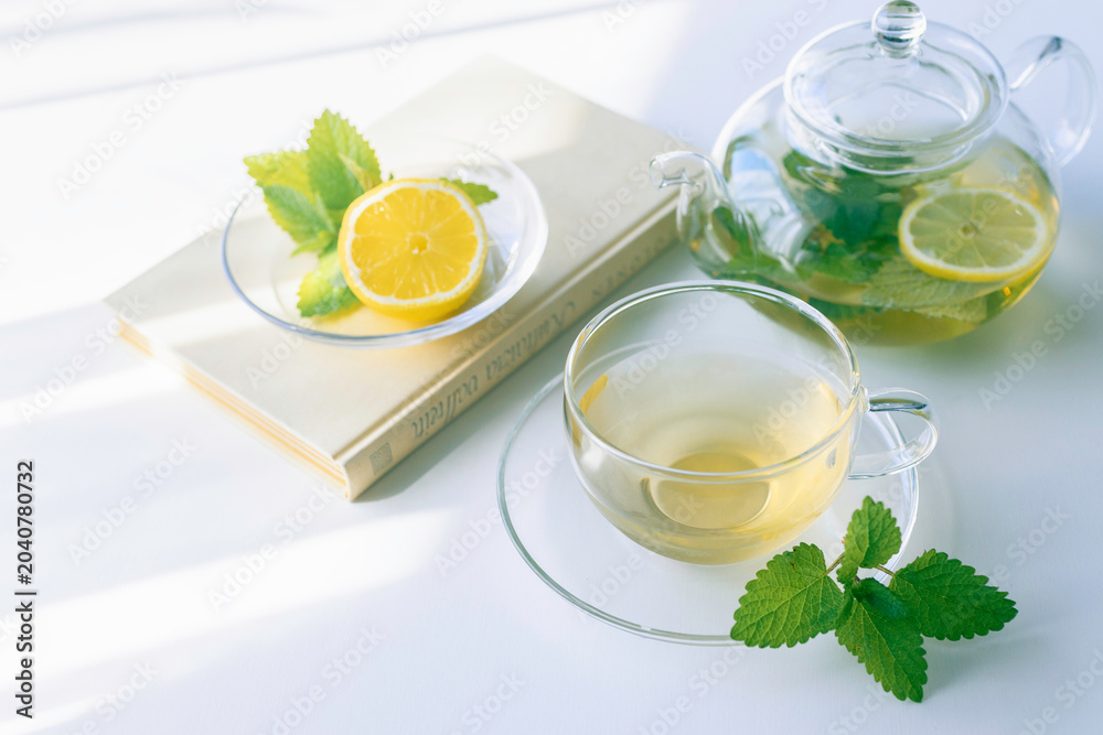 Fototapeta premium Book and fresh mint herbal tea with lemon on a bright table