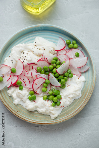 Salad with fresh radish, green peas and torn burrata on a turquoise plate, vertical shot on a light-grey granite background, high angle view