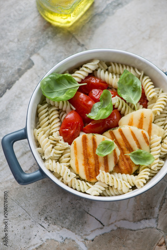 Fusilli pasta with slices of grilled haloumi cheese and tomatoes, vertical shot on a grey granite background, high angle view
