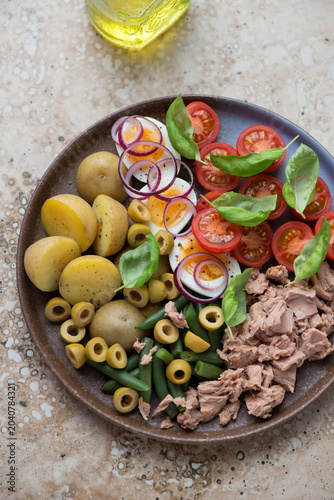 Brown plate with nicoise or french salad with tuna, vertical shot on a beige granite background, middle closeup