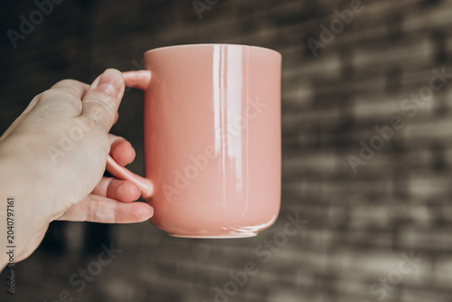 Hand Holding Pink Coffee Mug Against Cozy Brick Wall Background
