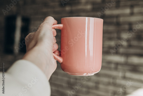 Hand Holding Pink Coffee Mug Against Cozy Brick Wall Background