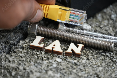 Wooden letters spell 'LAN' as a hand holds an Ethernet cable near a PoE injector.