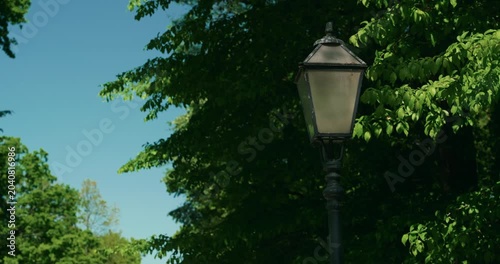 Vintage street lamp surrounded by green trees in Maksimir Park on a sunny day during Labor Day holiday.