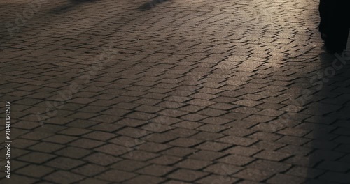 People walking across a cobblestone street casting long shadows during sunset in Zagreb Croatia.