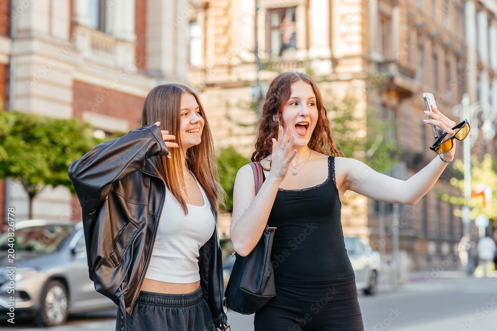 Fototapeta premium Two young women taking selfie with smartphone on city street outdoors