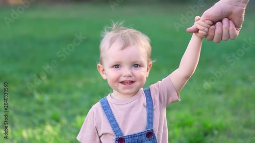 A happy toddler walks with his father hand in hand and smiles